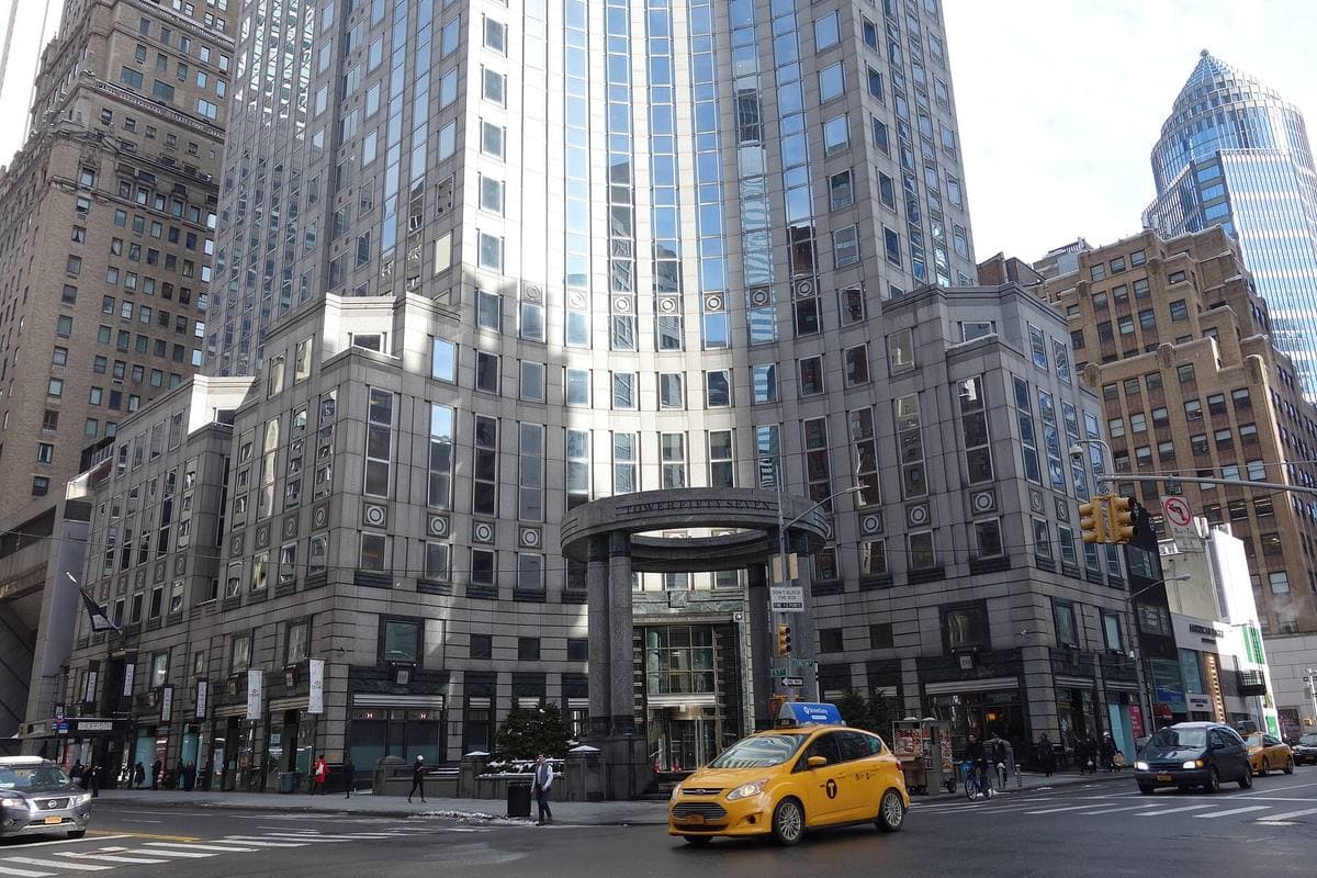 A curved glass tower behind a ring of tall columns on a Midtown corner