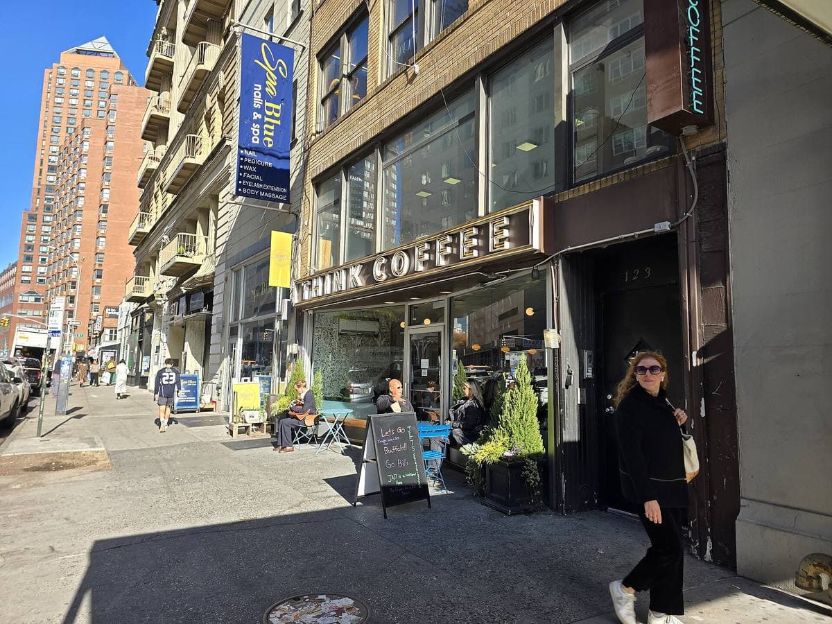 A café front with outdoor tables on a sunny Manhattan avenue