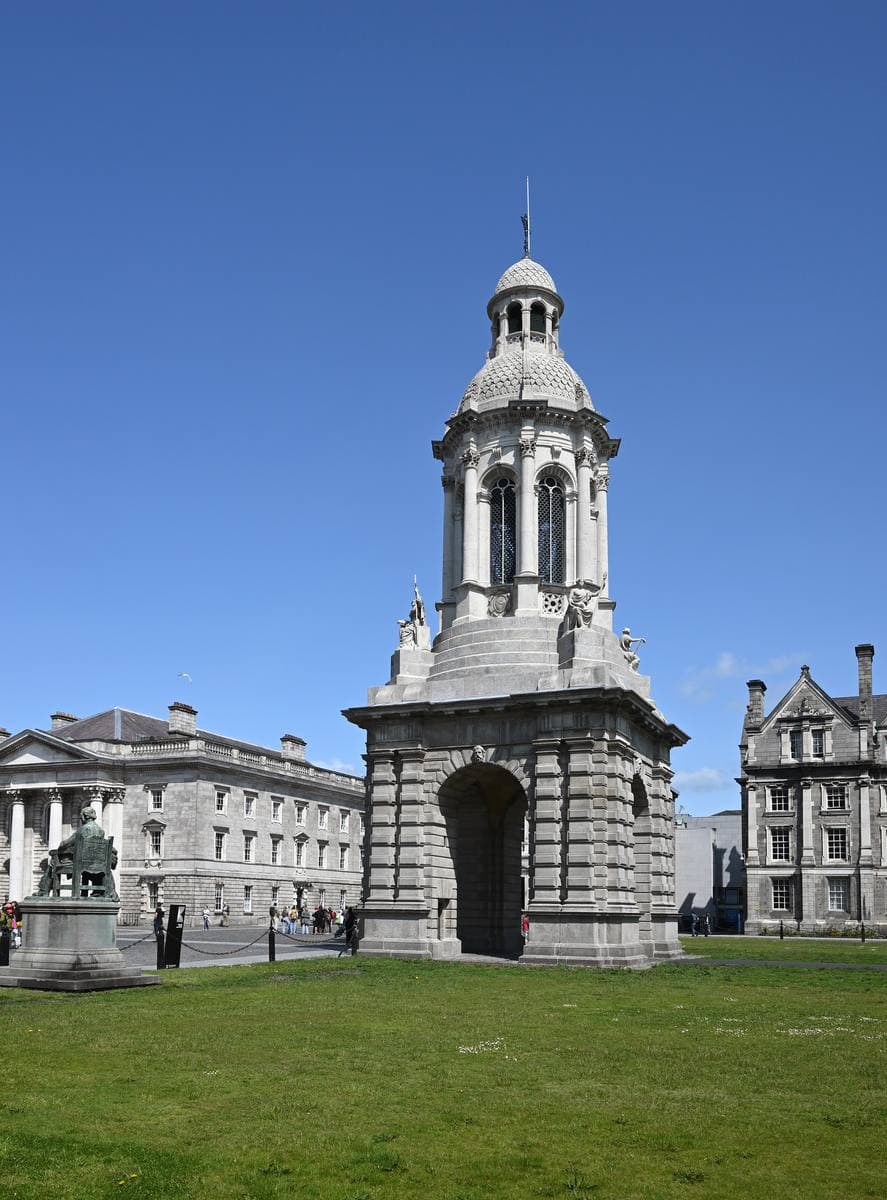 A tall stone bell tower with arches and a domed top, on a lawn under a blue sky