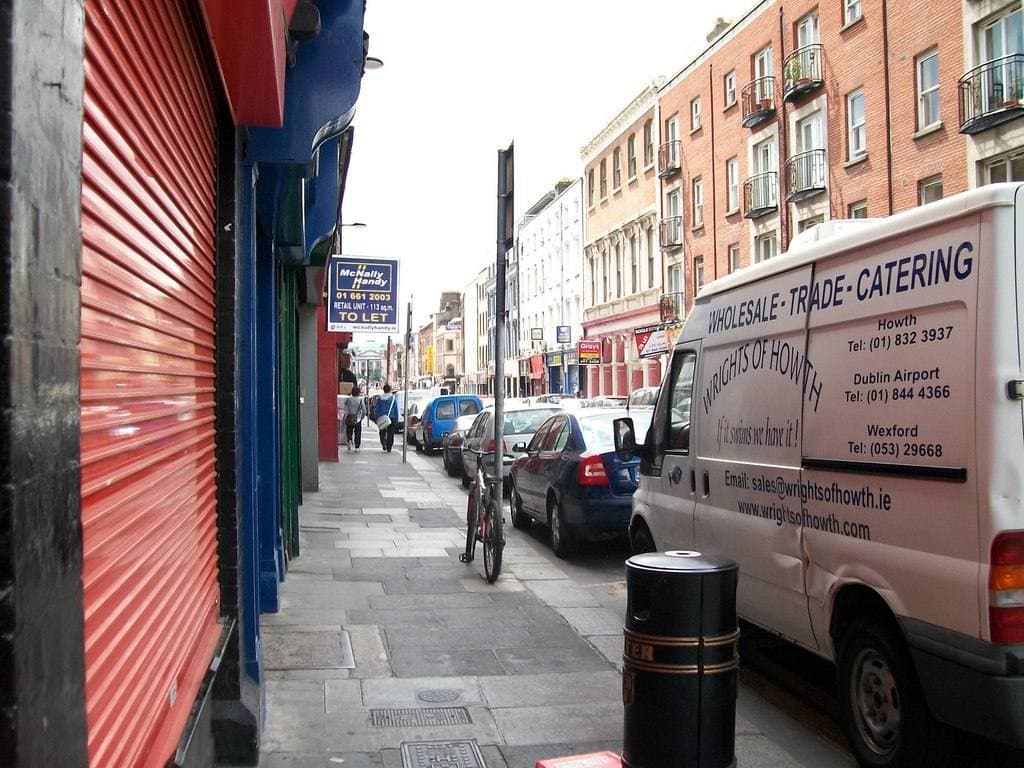 A city street of brick buildings, parked cars and a red shop shutter