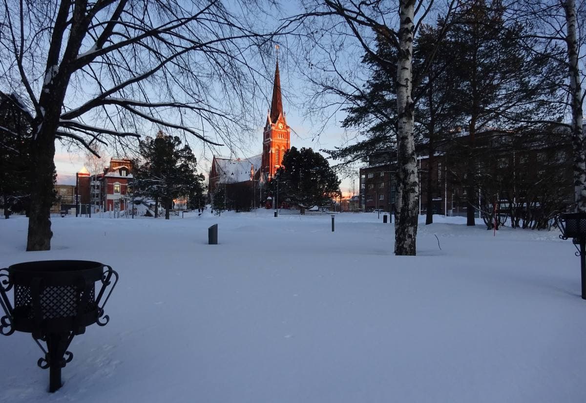 A red-brick church spire behind snowy lawns and bare birch trees