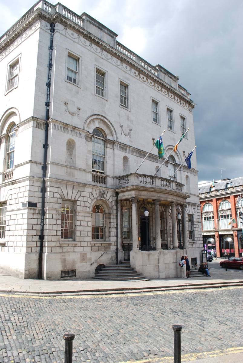 A white Portland-stone Georgian building with a columned porch on a cobbled corner