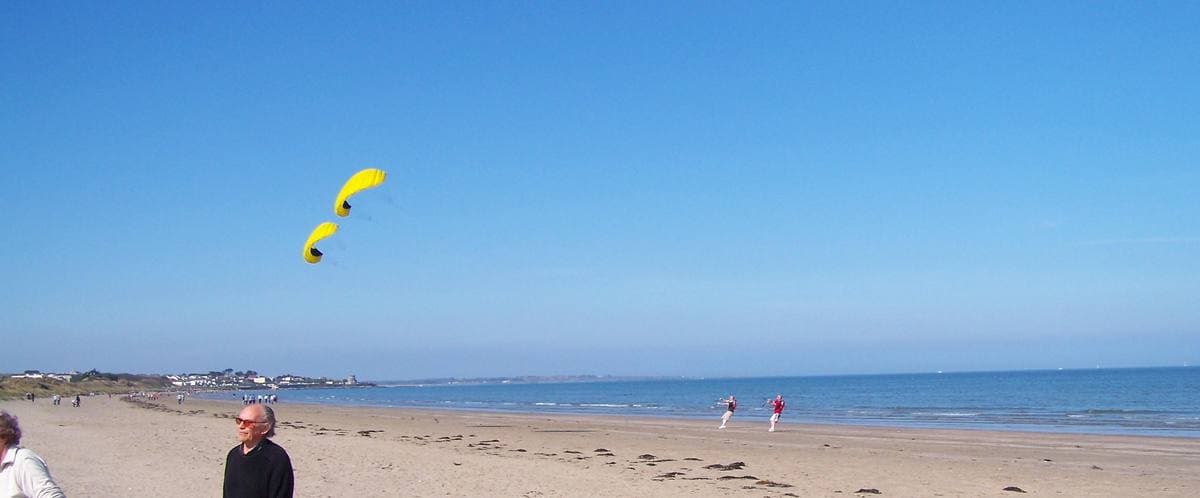 A long sandy beach under a blue sky, with yellow kites in the air