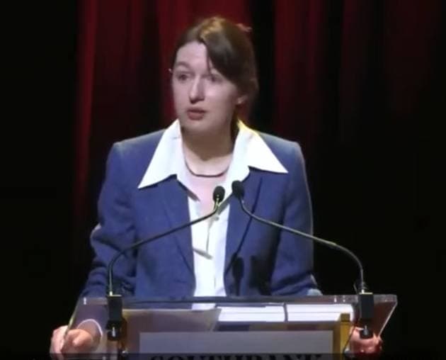 Sally Rooney in a blue jacket and white collar at a lectern