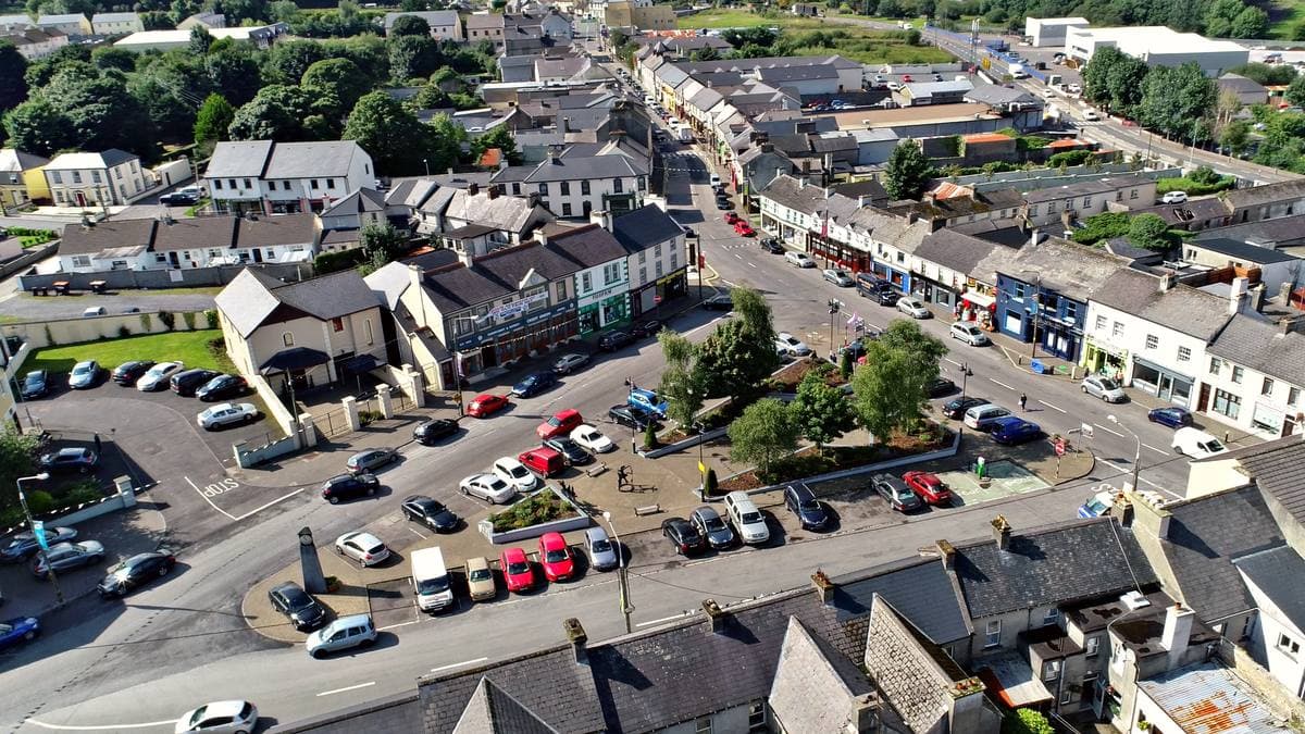 An aerial view of a small Irish town square full of parked cars, ringed by two-storey shops