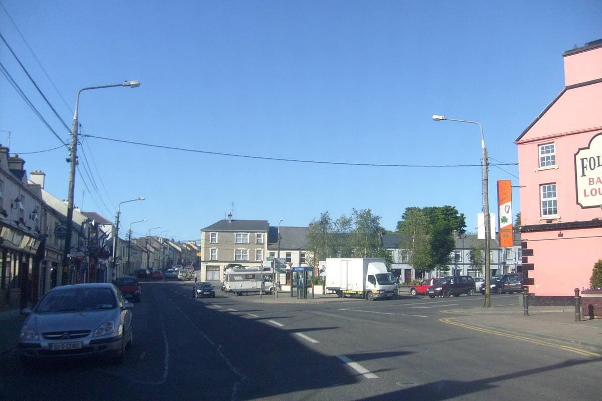 A wide main street of painted shopfronts and parked cars under a blue sky