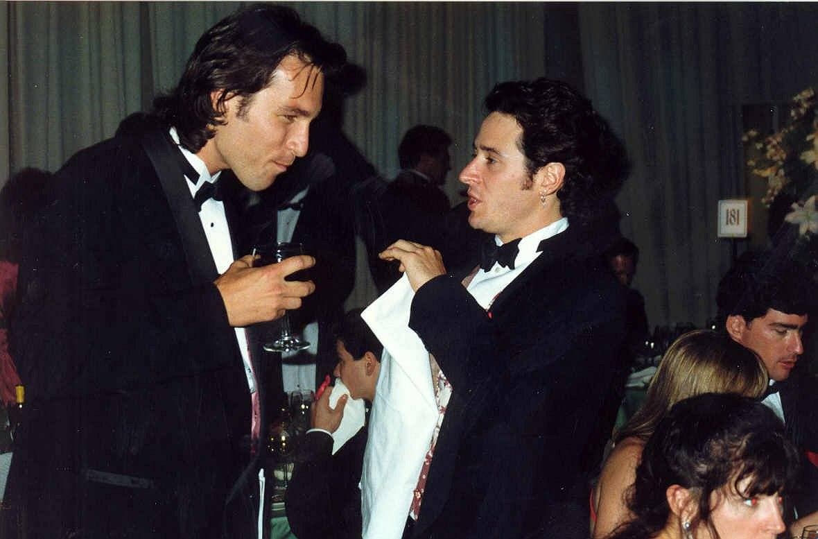 Two men in dinner jackets talking at a crowded party