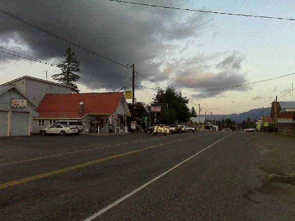 A wide empty road through a small mountain town under a cloudy sky
