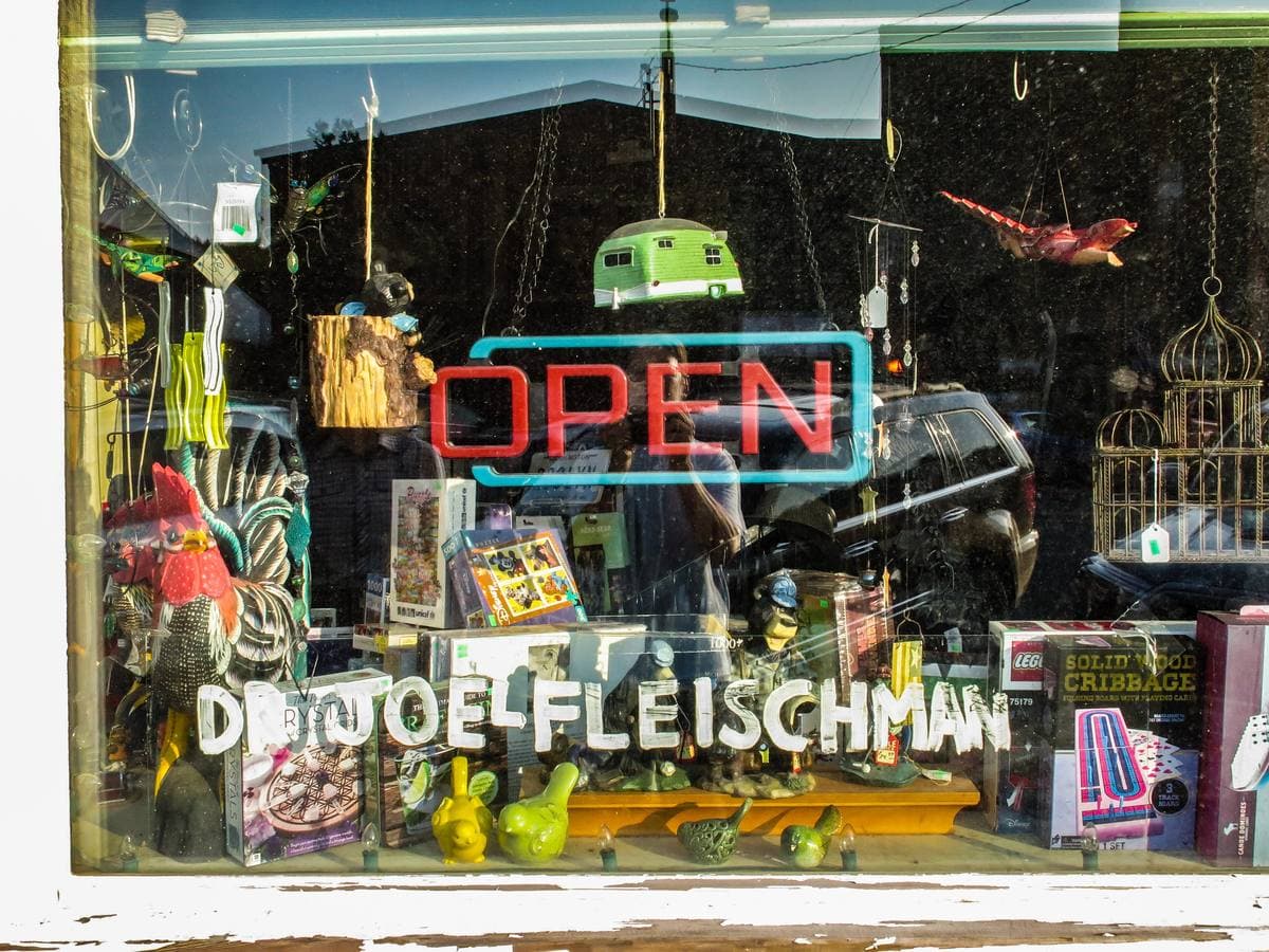 A shop window full of gifts with an Open sign and the painted name Dr Joel Fleischman across the glass