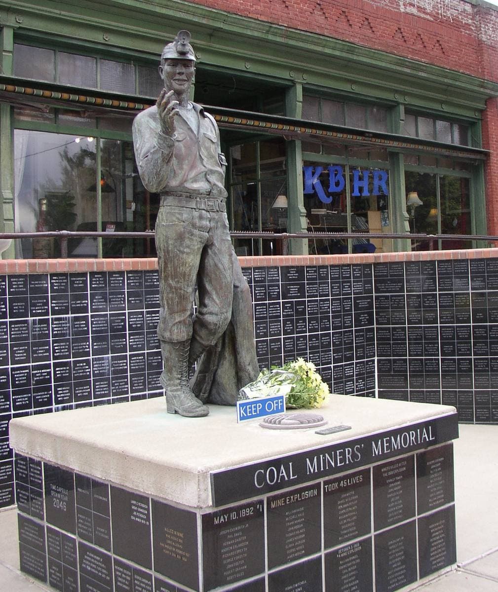 A bronze miner statue on a black plinth in front of a shop window lettered KBHR