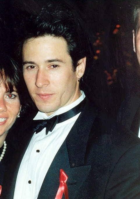 A young dark-haired man in a dinner jacket and bow tie, smiling