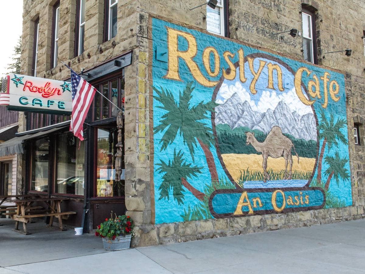 The camel mural on the side of a stone building, with the café’s neon sign and a flag at the corner