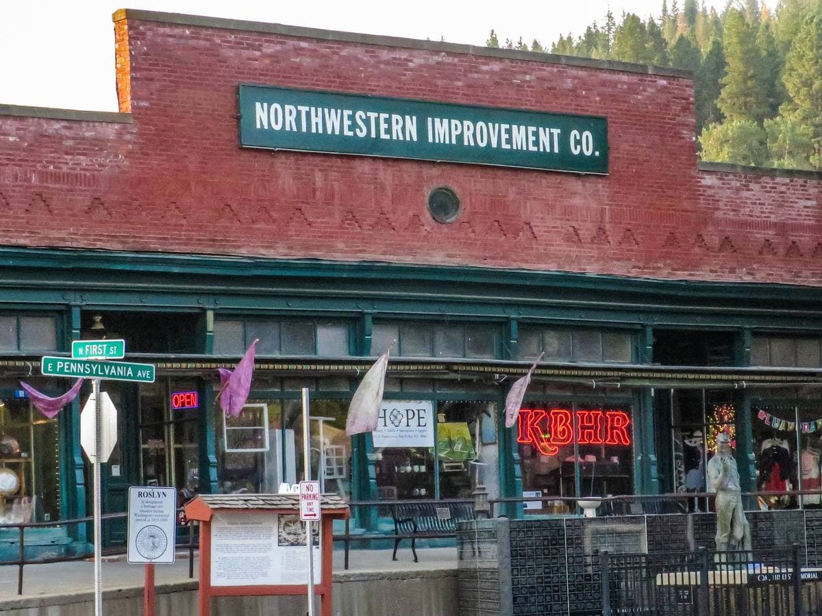 A long red brick store front with a green Northwestern Improvement Co. sign and flags along the pavement