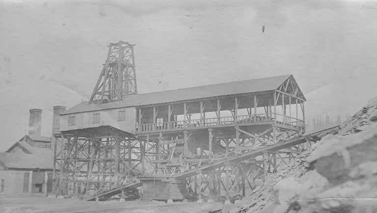 A faded photograph of a wooden mine head frame and a long timber tipple on a slope