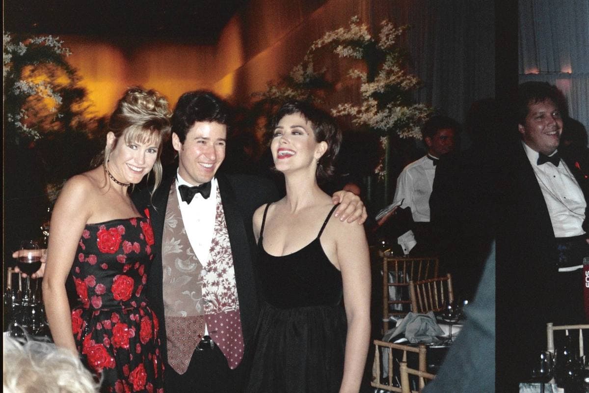 Two women and a man in evening dress standing arm in arm at a party