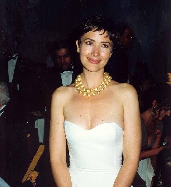 A woman with short dark hair in a white strapless dress and a gold necklace