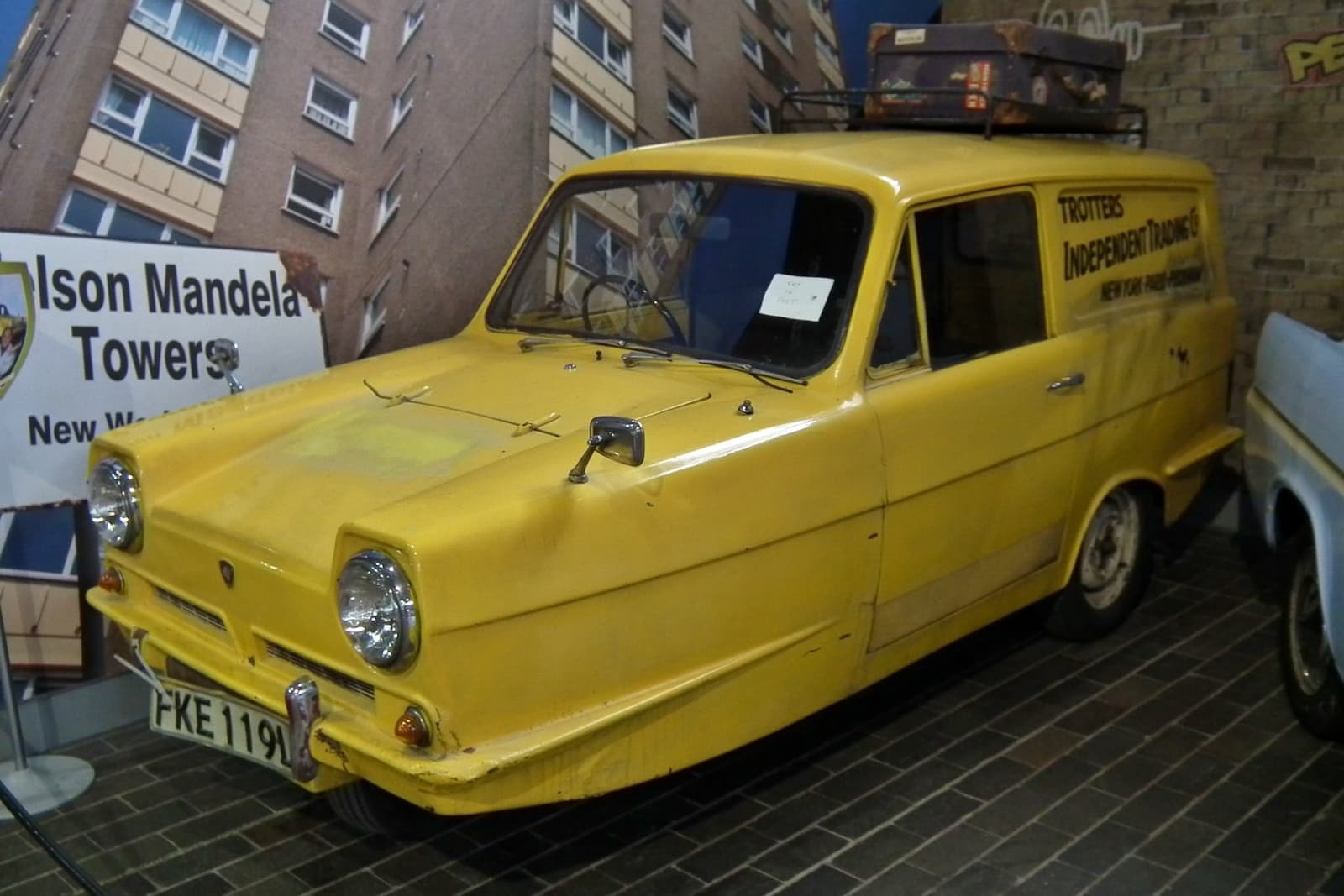 A yellow three-wheeled van in a museum display beside a tower-block sign