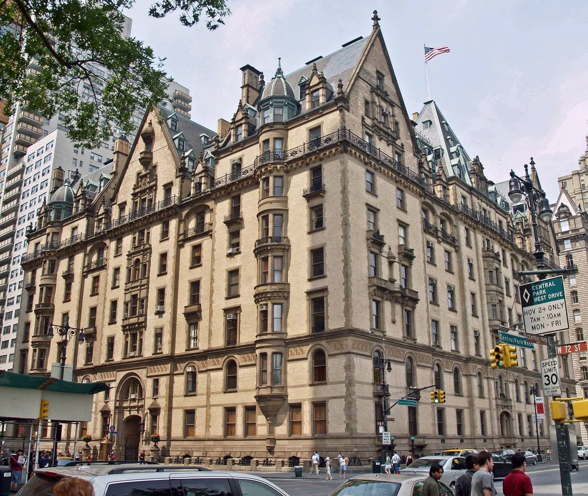 A tall gabled yellow-brick apartment building with dormers and turrets on a sunny corner of Central Park West