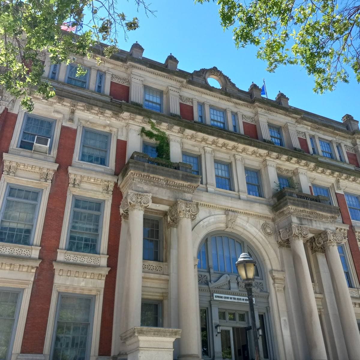 A red-brick and limestone courthouse with columns, arched windows and a grand doorway under a blue sky