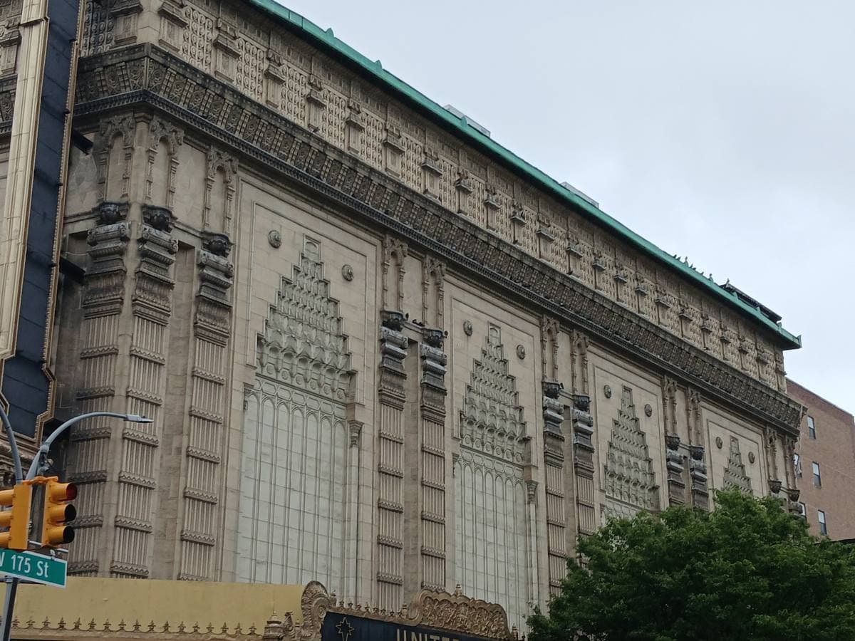 A huge windowless theatre wall covered in carved stone ornament in tall pointed panels, seen from a street corner with traffic lights