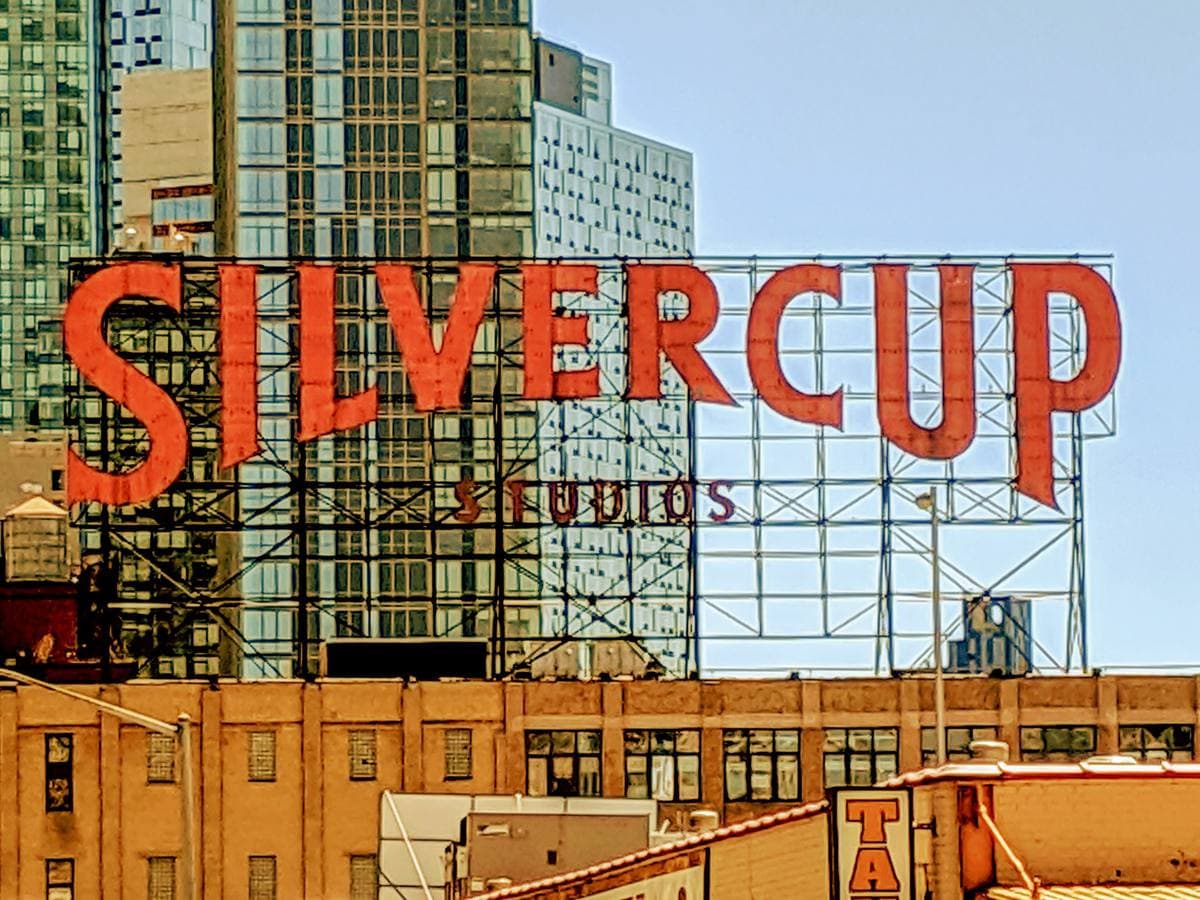 Giant red rooftop letters spelling Silvercup on a steel frame above an old brick factory, with towers behind