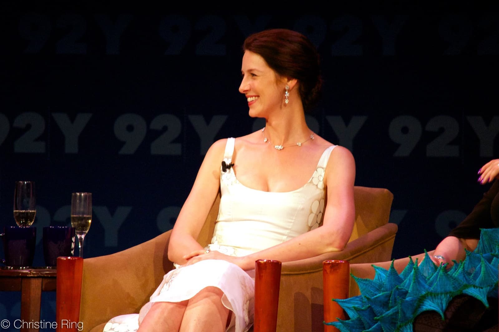 Caitríona Balfe smiling, seated on stage in a white dress