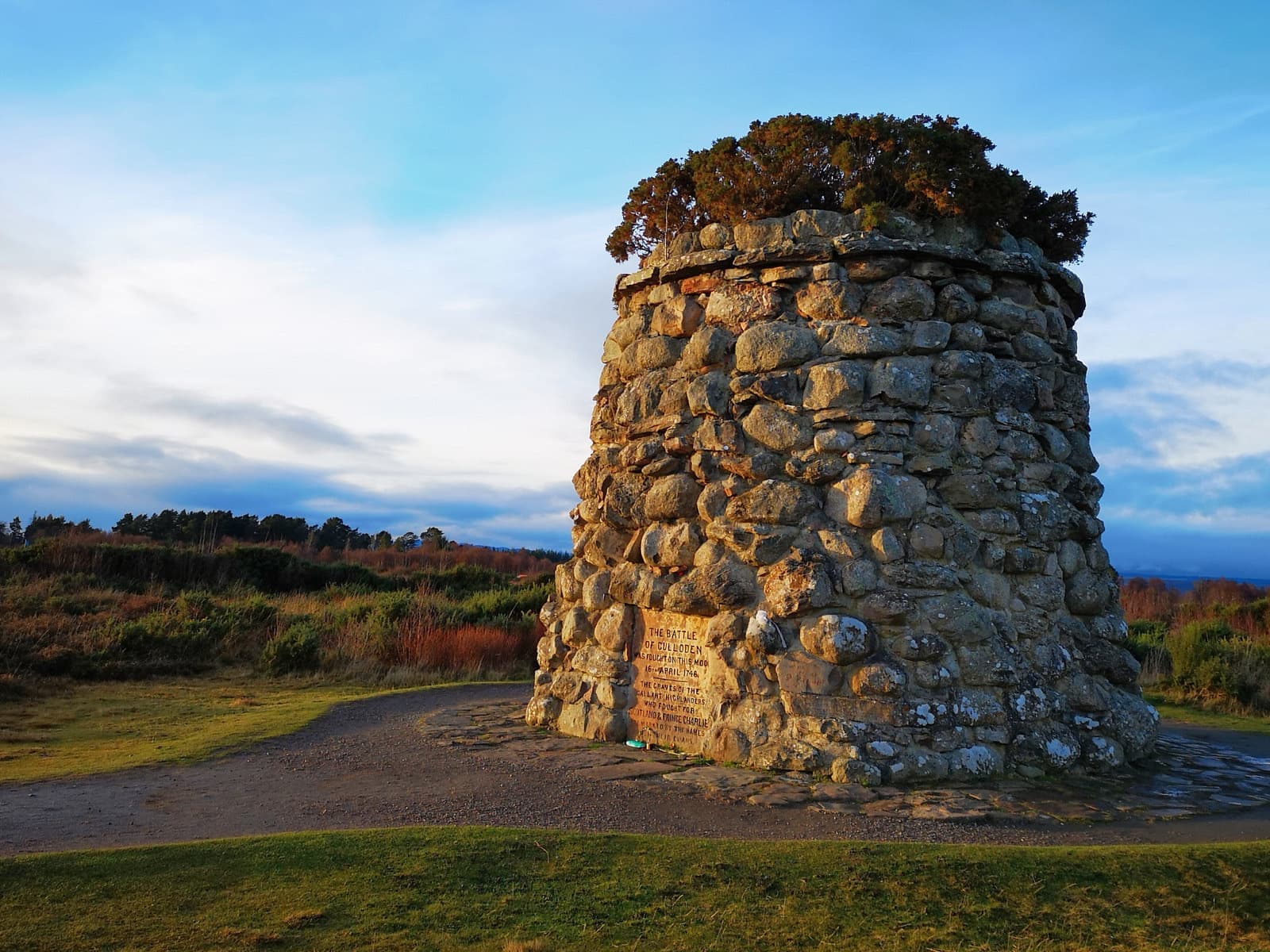 A round stone memorial cairn on moorland under a blue sky
