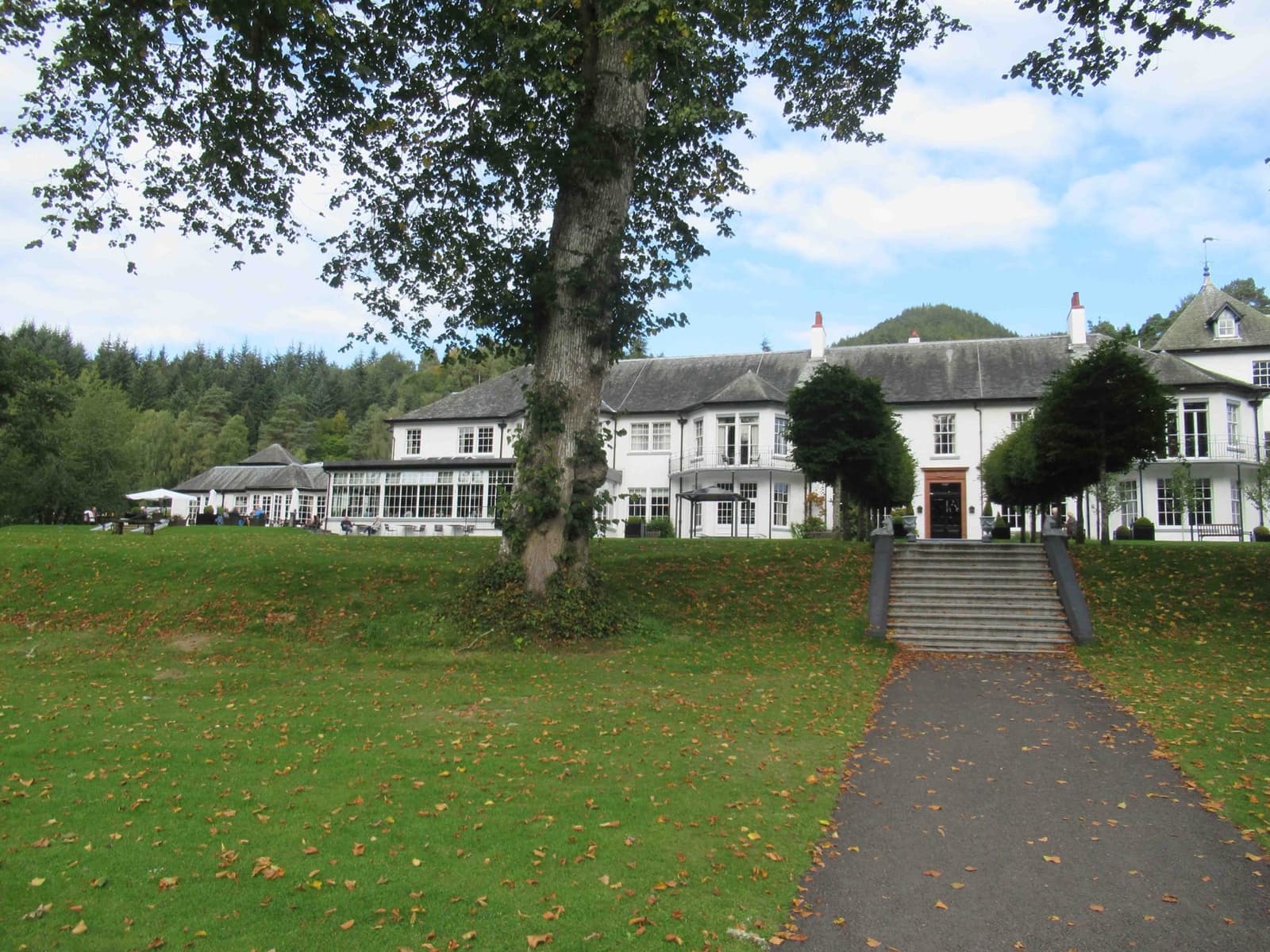 A long white country-house hotel across a lawn with a tree in front