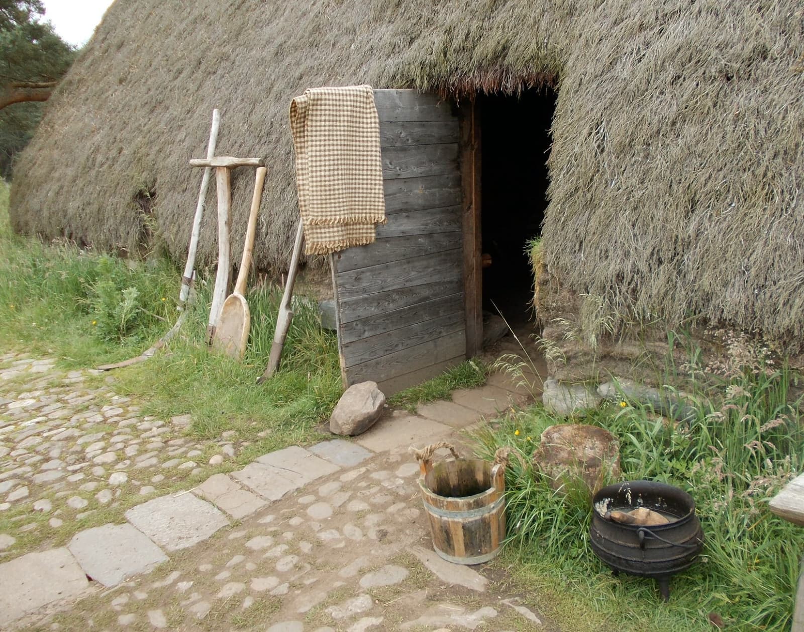 A low turf-and-thatch house with wooden tools leaning at the door