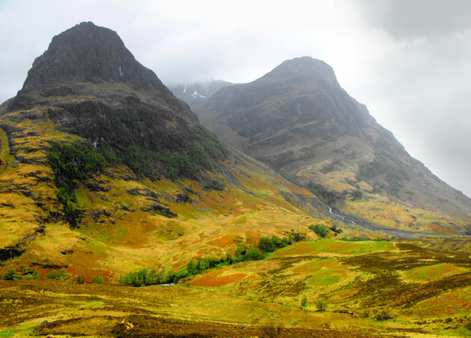Steep green and gold mountain buttresses in Glen Coe under cloud