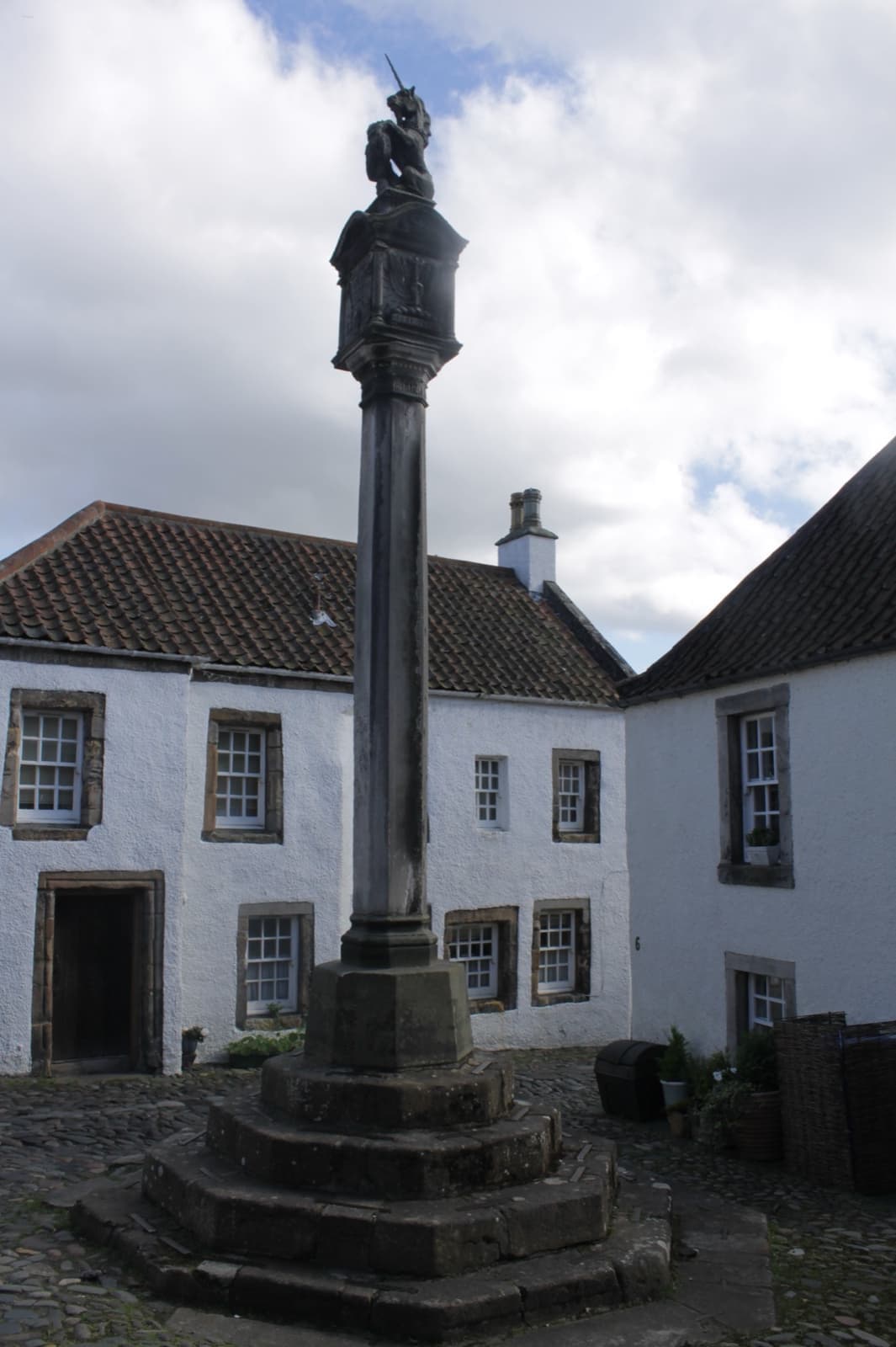 A stone market cross on stepped base in front of white harled houses