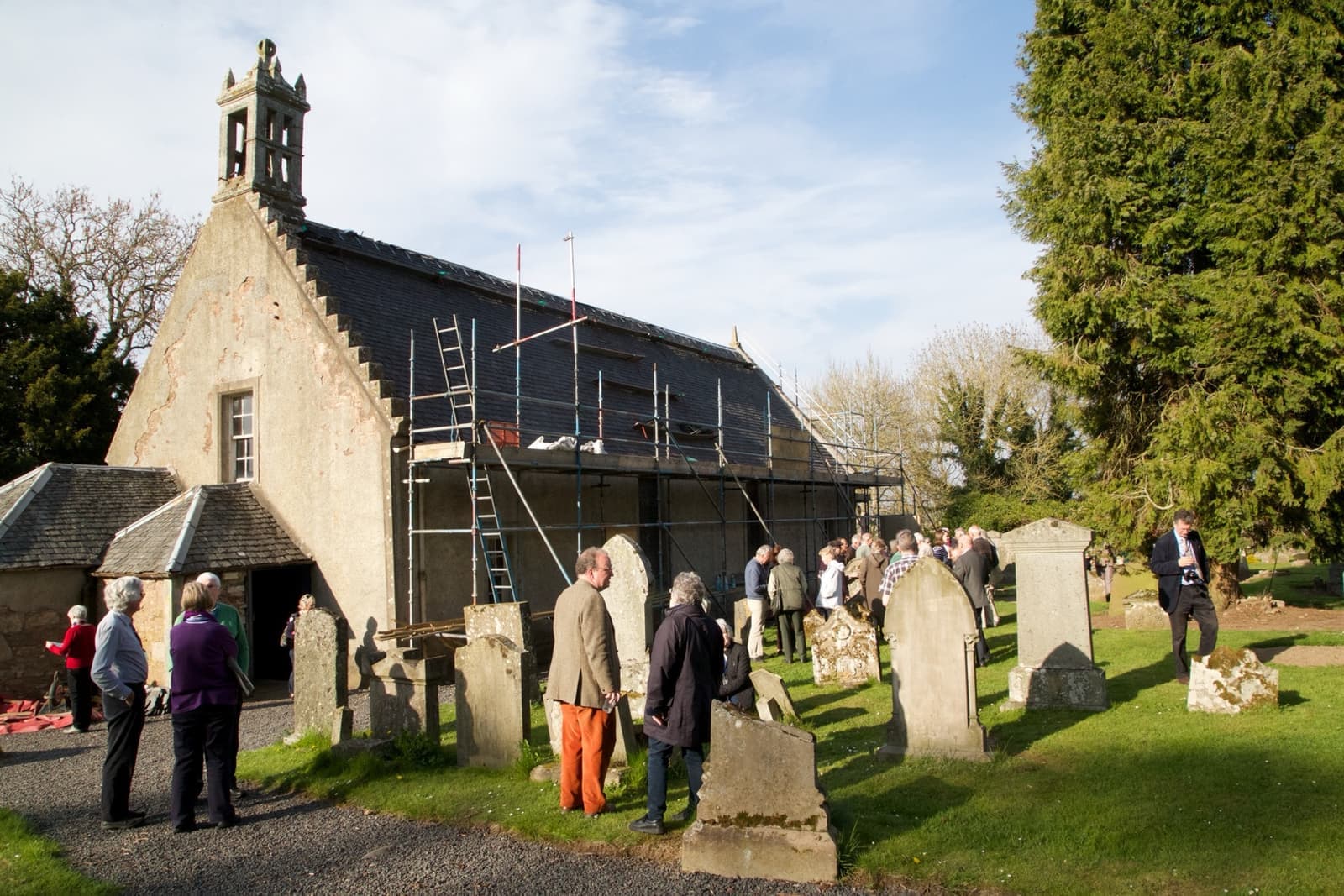 A small harled church with a bellcote among old gravestones