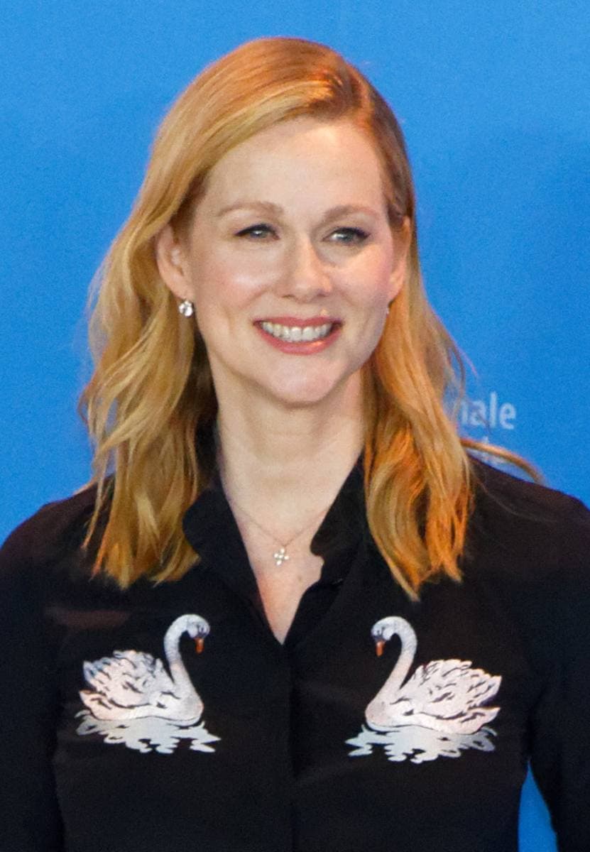 Laura Linney smiling, with long red-blonde hair, in a black blouse embroidered with two white swans