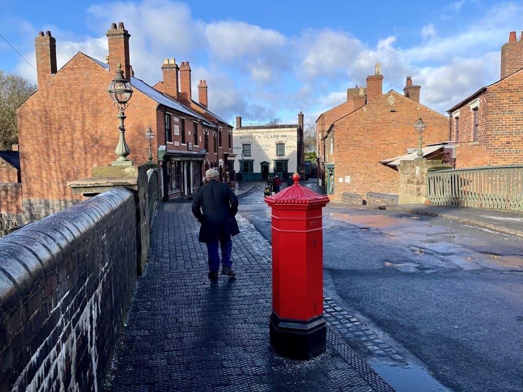 A wet blue-brick street with a red pillar box running down to brick houses