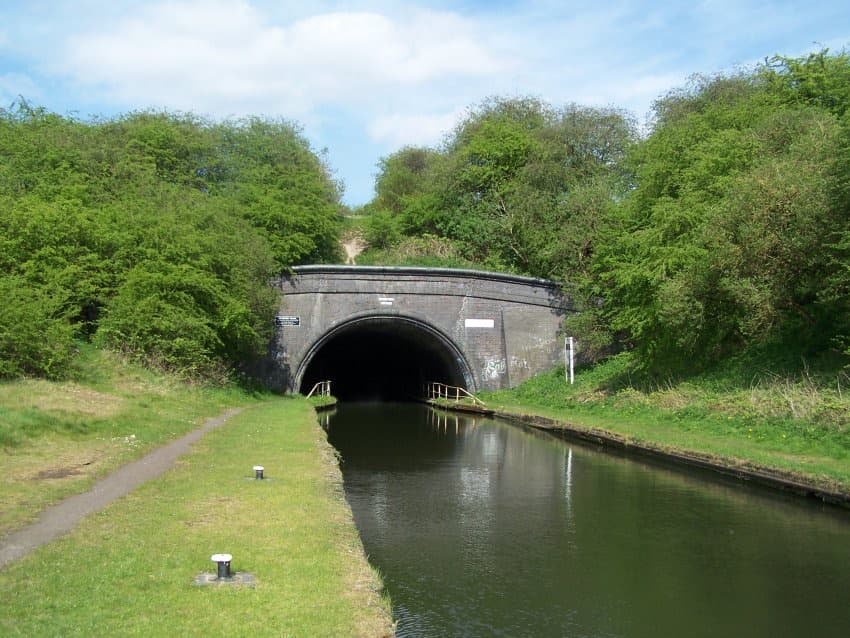 The brick mouth of a canal tunnel with a towpath beside the water