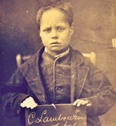 A boy holding a slate with his name chalked on it in a sepia police photograph