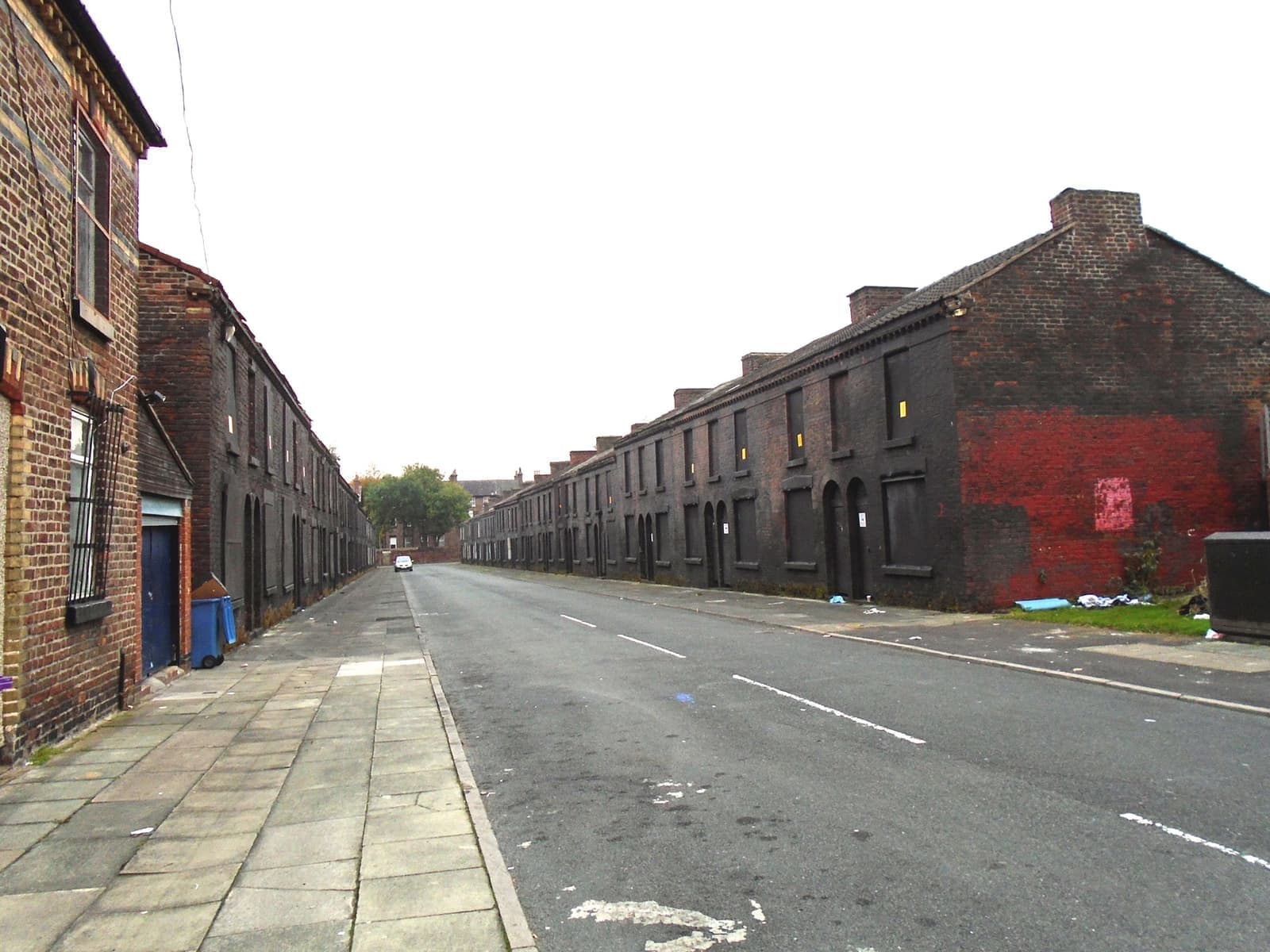 A long, empty terraced street with blackened brick house fronts