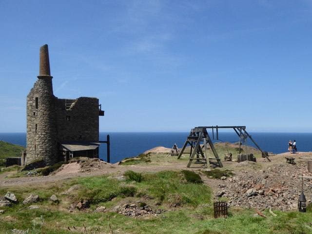 A ruined engine house and a timber headframe built as a film set on the cliff top, with the sea behind