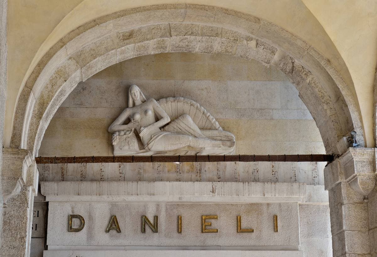 A carved stone lunette with a reclining figure above a plaque reading DANIELI