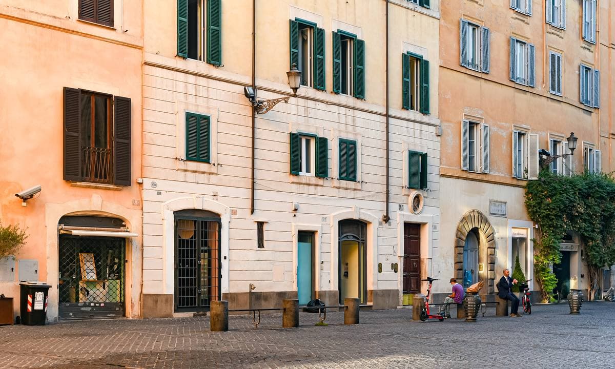 A row of shuttered palazzi with café tables along a quiet Roman square
