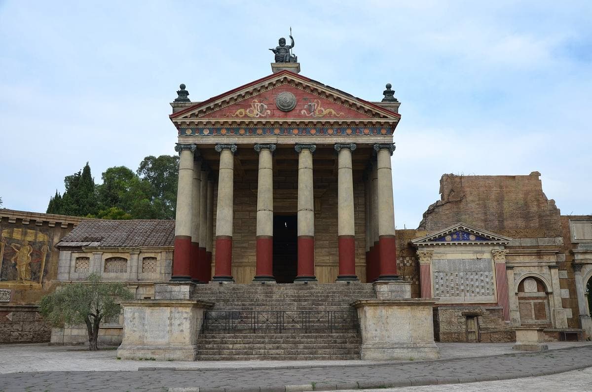 A painted temple front with red and white columns at the top of a flight of steps