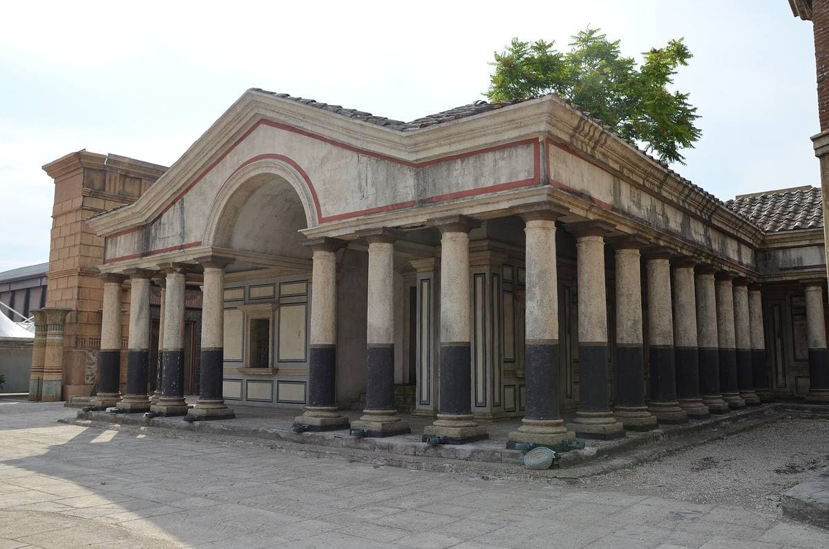 A long two-storey arcade with round arches and dark red columns