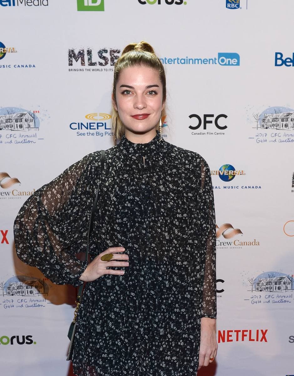 Annie Murphy, hair up, in a dark patterned dress, smiling on a red carpet