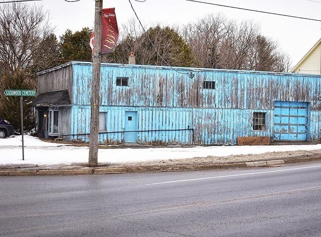A long pale-blue corrugated workshop on a snowy Goodwood street