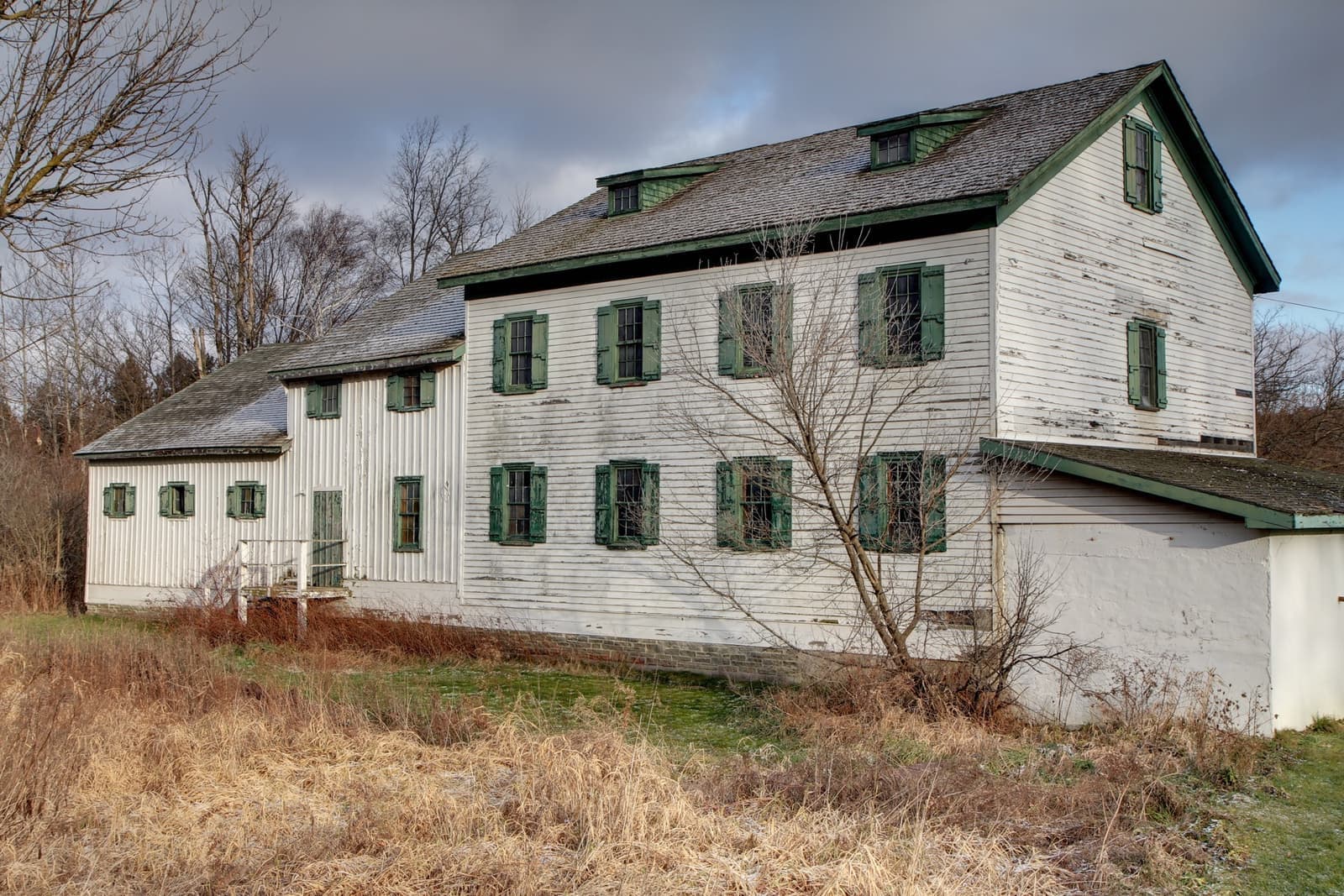 A white clapboard mill with green shutters in winter grass