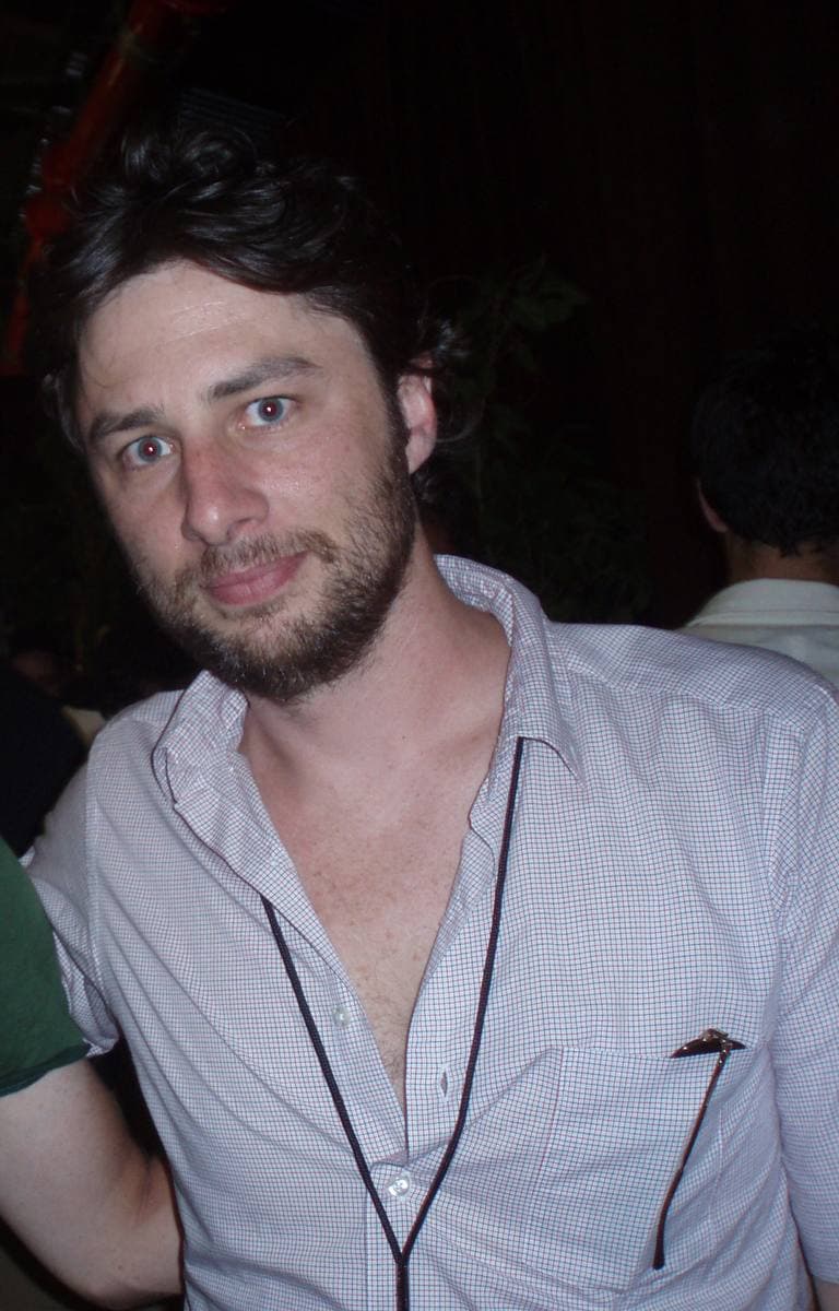A smiling man with stubble in an open-necked white shirt with a lanyard