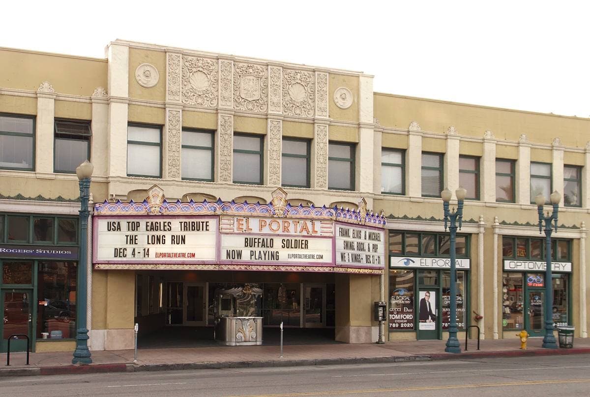 A cream 1920s theatre front with a red-lettered marquee and a corner box office on a sunny street