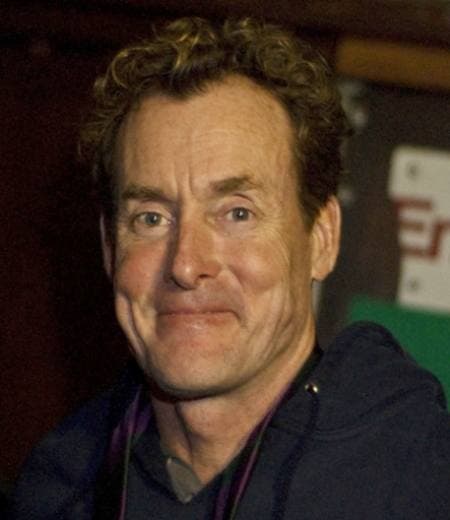 A man with curly greying hair and a crooked grin