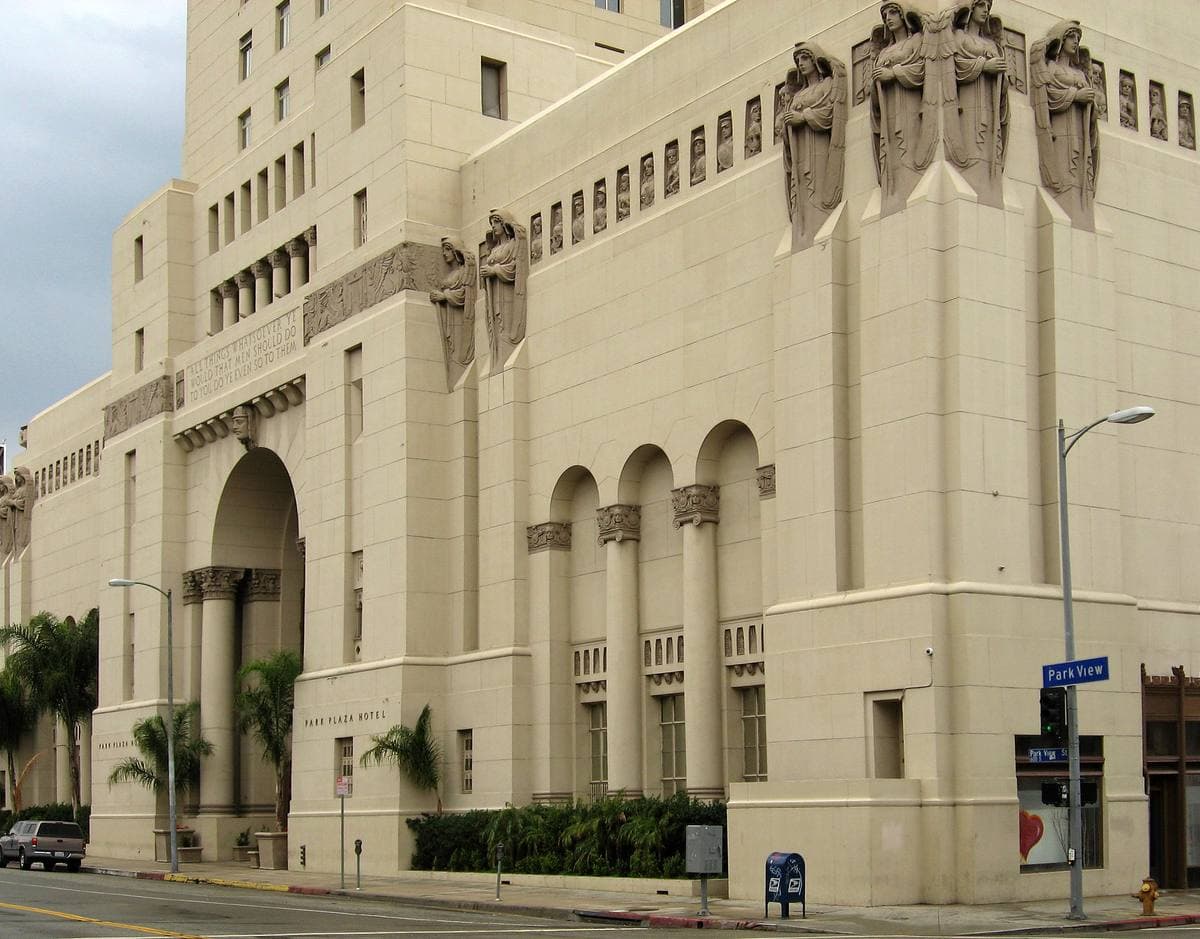 A tall cream stone building with deep arched windows and carved figures high on its corners