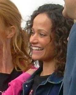 A smiling woman with dark curly hair in a denim jacket